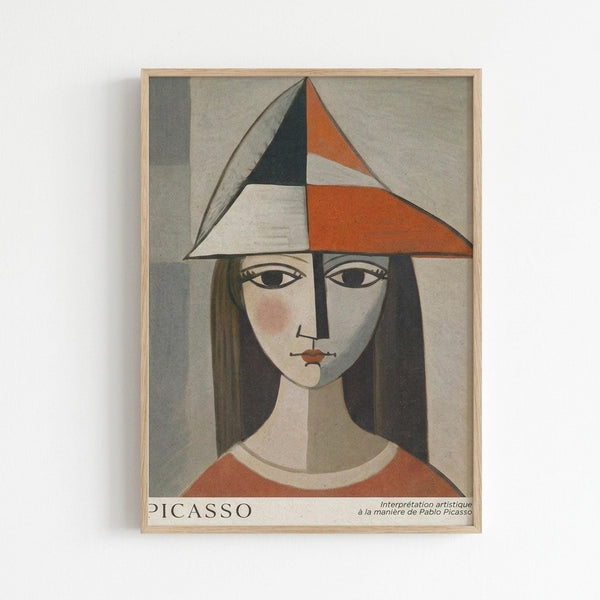 Framed art print featuring a cubist-style portrait of a woman with geometric angular features. She wears a triangular hat in orange, black, white and gray segments, with long dark hair framing her stylized face. Her orange top contrasts against the muted gray background. The piece shows fragmented planes and asymmetrical composition typical of modernist portraiture. Text at bottom reads "PICASSO" and "Interprétation artistique à la manière de Pablo Picasso" in a light wooden frame agains