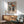 May include: Framed Picasso-style cubist portrait poster of woman wearing geometric angular hat in orange, black and white triangular shapes, displayed above wooden sideboard with table lamp, next to sage green mid-century armchair in modern living room with natural sunlight casting shadows on white wall.