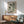 May include: Framed poster showing four black cat silhouettes in different playful poses on sage green and cream geometric background, displayed above wooden sideboard with white ceramic lamp in modern living room with mint green mid-century armchair and natural sunlight casting shadows on white wall.