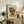 May include: Framed Picasso-style cubist portrait poster with geometric colorful face design displayed on rustic wooden sideboard alongside fern plant, books, ceramic vase, and beige armchair in modern living room setting with neutral walls