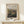 May include: Framed art print featuring Pierre Auguste Renoir's impressionist landscape painting of rolling hills and countryside around Berneval, displayed on light wood console table with small white gift box tied with evergreen sprig, set against cream wall with natural lighting