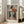 May include: Framed poster with Picasso-style cubist portrait of woman wearing geometric triangular hat in orange, black and gray tones, long dark hair, pale face with stylized features, displayed on light wooden floor next to beige upholstered chair in bright sunlit room with white walls and large windows.