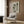 May include: Framed poster print featuring four black cat silhouettes in different playful poses displayed above a beige upholstered armchair with geometric patterned pillow. Modern reading nook with gold floor lamp, dark round side table with open book, wood panel wall, and natural light from window with sheer curtains.