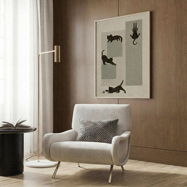 May include: Framed poster print featuring four black cat silhouettes in different playful poses displayed above a beige upholstered armchair with geometric patterned pillow. Modern reading nook with gold floor lamp, dark round side table with open book, wood panel wall, and natural light from window with sheer curtains.