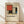 May include: Framed exhibition poster featuring a geometric abstract composition with red, blue, yellow, black and beige rectangular shapes in Mondrian's distinctive style. The cream-colored poster displays black text below the artwork. Shown in a light wooden frame leaning against a white wall on wooden flooring with soft natural lighting creating diagonal shadows.
