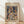 May include: Framed Paul Klee abstract art print leaning against white wall on light wooden floor. The colorful geometric artwork features mosaic-like squares and shapes in blues, greens, oranges, purples and earth tones, creating fragmented architectural forms. Natural wood frame with cream matting. Soft window light creates diagonal shadows across the white textured wall behind the medium-sized poster.