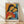 May include: Framed abstract art print in wooden frame leaning against white wall on light wood floor. Artwork shows two stylized figures with dark hair embracing, rendered in vibrant oranges, blues, and reds with geometric facial features. French text at bottom reads "Art contemporain inspiré par un maître artistique" and "PICASSO". Natural lighting creates soft shadows on textured white wall.