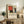 May include: Framed geometric art print with red, blue, yellow, black and beige rectangular blocks in modernist style, displayed on rustic wooden sideboard alongside potted fern, ceramic vase, stacked books, and cream upholstered chair in neutral-toned living room setting.