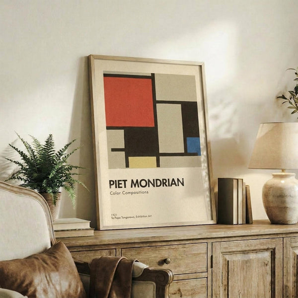 May include: Framed geometric art print with red, blue, yellow, black and beige rectangular blocks in modernist style, displayed on rustic wooden sideboard alongside potted fern, ceramic vase, stacked books, and cream upholstered chair in neutral-toned living room setting.