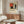 May include: Abstract geometric art poster featuring red, blue, yellow, black and beige rectangular shapes in Mondrian style, displayed above wooden sideboard in modern living room with white curved chair, glass coffee table, and brass floor lamp