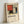 May include: Framed art print featuring geometric abstract composition with red, blue, yellow, black, gray and white rectangular shapes divided by bold black lines in Mondrian style, displayed in light wood frame leaning against white wall on white surface