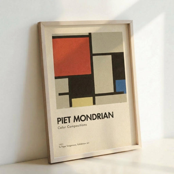 May include: Framed art print featuring geometric abstract composition with red, blue, yellow, black, gray and white rectangular shapes divided by bold black lines in Mondrian style, displayed in light wood frame leaning against white wall on white surface