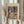 May include: Person in cream ruffled sleeves holding framed Paul Klee art print featuring abstract geometric composition in colorful squares, triangles and botanical motifs. Light wood frame against soft neutral background with dried pampas grass stems visible on left side.