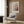 May include: Paul Klee exhibition poster displayed in modern reading nook with beige upholstered armchair, geometric patterned pillow, brass floor lamp, and dark round side table with open book. The framed artwork features abstract circular forms in pink and orange tones with dotted patterns against wood-paneled wall. Soft natural lighting from nearby window illuminates the cozy corner setup on hardwood flooring.