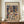 May include: Framed Paul Klee abstract art print displayed on wooden sideboard against cream wall with white ceramic vase and stacked books. The colorful geometric artwork features fragmented architectural forms in muted blues, oranges, purples and greens with botanical motifs. Museum exhibition poster in natural wood frame on elegant furniture piece.