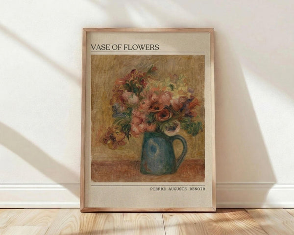 May include: Framed art print featuring Pierre Auguste Renoir's impressionist painting of colorful flowers in a blue-green ceramic pitcher. The artwork shows soft brushstrokes with pink, orange, and red blooms against a warm golden background. The print has cream matting with the title "VASE OF FLOWERS" at top and artist name at bottom, displayed in a light wood frame leaning against white walls on natural wood flooring with sunlight streaming across the scene.