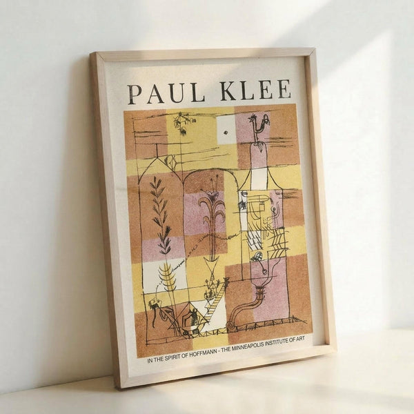 May include: A framed poster print leaning against a white wall, featuring Paul Klee's abstract artwork in warm yellows, oranges, browns, and pinks with geometric shapes and whimsical line drawings of plants and figures. The artwork shows a mosaic-like composition with botanical elements and playful characters scattered throughout colored rectangular sections. Text at bottom reads "In the Spirit of Hoffmann - The Minneapolis Institute of Art." Light wood frame surrounds the print on cream-colo