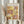 May include: Person in cream ruffled sleeves holding framed Paul Klee exhibition poster featuring abstract geometric composition in warm yellows, oranges, and pinks with botanical line drawings, alongside dried wheat stems against soft white curtained background