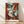 May include: Framed abstract cubist-style portrait poster featuring a deconstructed face with geometric shapes in vibrant orange, teal, cream and red tones. The artwork shows fragmented facial features including an eye, lips and angular planes in Picasso-inspired style. Natural wood frame displays against white wall on light wooden flooring with soft window lighting creating diagonal shadows across the scene.