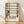 May include: Framed art print leaning against white textured wall on light wooden floor with soft natural lighting. The artwork features geometric abstract composition with black grid lines, cream background, and colored rectangles in yellow, red, and blue. Text below reads "PIET MONDRIAN" and "1872-1944 Trafalgar Square" in serif font. Natural wood frame visible around edges.
