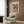 May include: Framed Paul Klee abstract art print featuring colorful geometric squares in reds, greens, violets, and earth tones, displayed on wood-paneled wall above beige upholstered armchair with geometric patterned pillow, brass floor lamp, and dark round side table with open book in modern living room setting