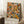 May include: Abstract expressionist style poster with vibrant orange, blue, yellow and green paint splatters and black lines in wooden frame, leaning against white wall corner next to wooden side table with white coffee cup and saucer, cream blanket draped nearby on white textured rug