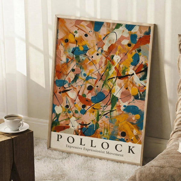 May include: Abstract expressionist style poster with vibrant orange, blue, yellow and green paint splatters and black lines in wooden frame, leaning against white wall corner next to wooden side table with white coffee cup and saucer, cream blanket draped nearby on white textured rug