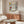 May include: Framed Piet Mondrian Trafalgar Square poster print featuring geometric black grid lines with yellow, red, and blue color blocks on cream background, displayed above mid-century modern walnut credenza in minimalist living room with white curved chair, brass floor lamp, and glass coffee table reflecting the artwork