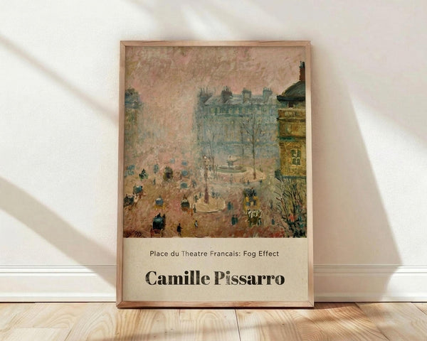 May include: Framed art print of Impressionist street scene showing foggy Parisian square with horse-drawn carriages, pedestrians, and Haussmanian buildings in muted pink and blue tones. Natural wood frame leaning against white wall on light wooden floor with soft window light casting shadows.