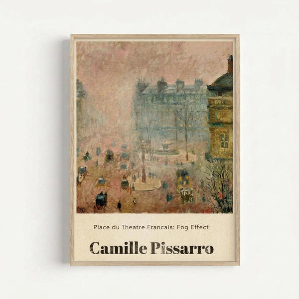 A framed art print displaying an Impressionist painting of a misty Parisian street scene with soft pink and beige tones. The artwork shows buildings, bare winter trees, horse-drawn carriages, and small figures of people walking through fog. Below the image is text reading "Place du Theatre Francais: Fog Effect" and "Camille Pissarro" in dark letters on a cream background. The print is mounted in a light wooden frame against a white wall.