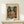 May include: Framed Picasso cubist artwork poster showing angular figure playing guitar in earth tones of brown, beige, and orange, displayed on light wooden console table next to small wrapped gift with greenery. Modern minimalist room setting with white walls and natural lighting creating soft shadows.