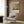 May include: Framed art print of Camille Pissarro's impressionist street scene with fog effect, showing Parisian buildings and figures in muted pink and blue tones. Print displayed on wood-paneled wall above beige upholstered armchair with geometric patterned pillow. Modern reading nook setting with brass floor lamp and side table.