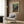May include: Paul Klee abstract art print with colorful geometric squares in blues, greens, reds, and yellows, displayed in light wooden frame on wood-paneled wall. Modern reading nook features cream upholstered armchair with geometric patterned pillow, brass floor lamp, and dark side table with open book. Natural light from window with sheer curtains illuminates warm neutral interior space.