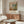 May include: Vintage-style art poster of Parisian street scene with buildings and figures in muted tones, displayed in thin frame above walnut wood credenza. Modern living room setting with cream curved chair, glass oval coffee table, and minimalist decor in neutral beige and wood tones.