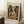 May include: Framed Picasso cubist artwork showing an abstract musician figure holding a guitar, rendered in earth tones of brown, beige, and muted colors. The poster leans against a white wall corner on a textured cream rug, with a coffee cup on a wooden block nearby and soft natural lighting creating shadows.