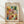 May include: Framed poster print featuring Paul Klee's abstract watercolor artwork with colorful geometric squares and rectangles in vibrant blues, greens, oranges, purples, and earth tones. The print shows "PAUL KLEE" at the top and "THE MET MUSEUM - 1914" at the bottom on cream-colored paper in a thin wooden frame, leaning against a white wall on light wooden flooring with natural sunlight casting diagonal shadows.
