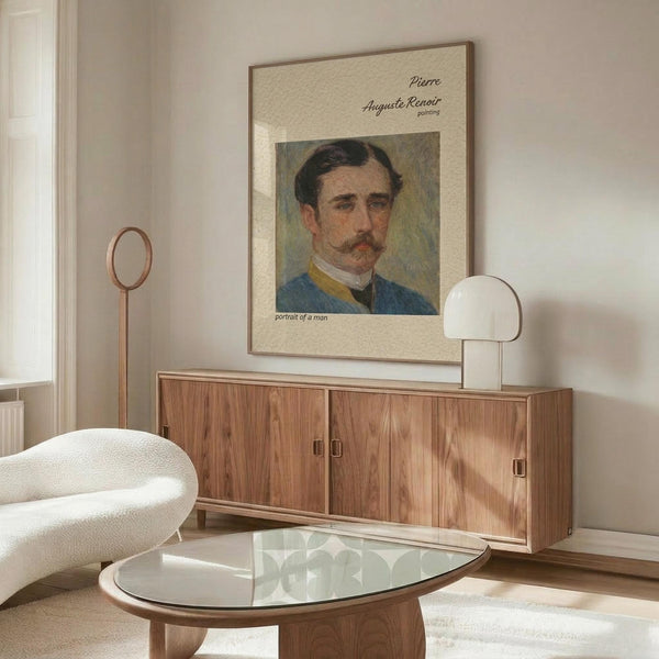 May include: Framed reproduction of Renoir portrait showing man with mustache in blue jacket, displayed above walnut credenza in minimalist living room with cream chair, glass coffee table, and white table lamp