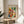 May include: Framed Paul Klee watercolor reproduction featuring colorful geometric squares in vibrant reds, blues, greens, yellows and purples arranged in a grid pattern. The museum poster sits on a round wooden side table next to a beige upholstered chair, with plant leaves casting shadows on white walls in soft natural lighting.