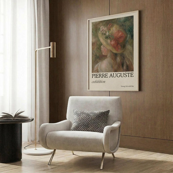 May include: Framed art poster featuring a young woman in a decorative hat with pink and green tones, displayed on wood-paneled wall above a cream upholstered armchair with geometric patterned pillow. Modern reading nook with brass floor lamp, dark round side table with open book, and natural lighting from nearby window with curtains.