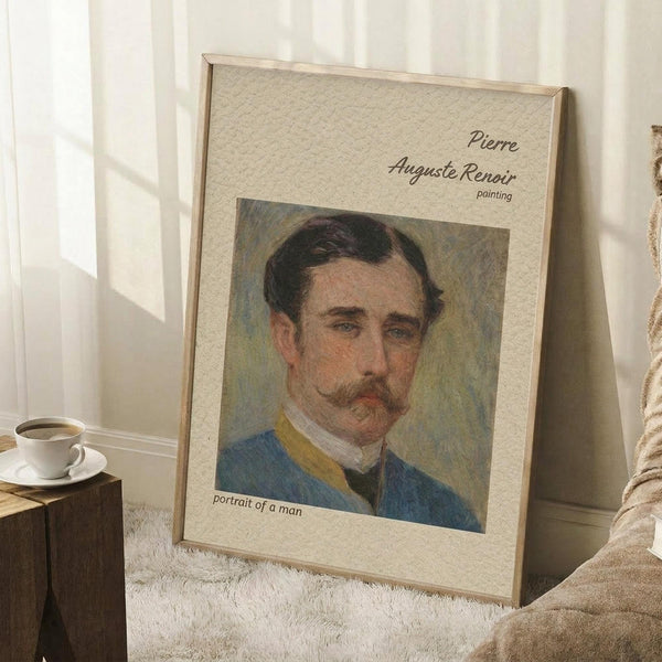 May include: Framed art print featuring a portrait of a man with dark hair and mustache wearing a blue jacket with yellow collar, displayed on white textured rug against white walls with window light, wooden side table with white coffee cup visible nearby