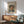 May include: Framed poster featuring a painted portrait of a man with dark hair and mustache wearing a blue jacket with yellow collar. The artwork is displayed above a wooden sideboard with table lamp in a modern living room setting with mint green upholstered chair and round coffee table. Warm natural lighting creates shadows across white walls.