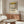 May include: Framed Piet Mondrian abstract art poster with geometric black lines and yellow, red, and blue color blocks, displayed above a mid-century modern wooden credenza. Scene shows minimalist living room with white curved chair, glass coffee table, and contemporary lighting fixtures against neutral beige walls.