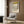 May include: Piet Mondrian exhibition poster with geometric black grid lines and colorful rectangles in yellow, red, and blue on cream background, displayed in modern living room with beige armchair, geometric patterned pillow, brass floor lamp, and wood-paneled wall