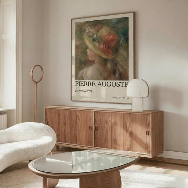 May include: Framed art print of a young woman wearing an ornate floral hat displayed above a mid-century modern walnut credenza with brass hardware. Room features cream walls, white upholstered chair, glass-top oval coffee table, and brass floor lamp. Print shows impressionist-style painting in soft greens, pinks, and earth tones with exhibition text below the image.