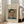 May include: Framed vintage portrait painting of a man with mustache wearing blue jacket, displayed in light wooden frame against beige textured mat, leaning against beige upholstered chair in bright sunlit room with white walls and large windows