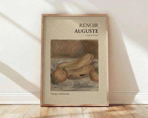 May include: Framed art print leaning against white wall on light wood floor with natural sunlight casting shadows. The poster features a warm-toned still life painting of oranges and bananas in muted yellows and browns, with "RENOIR AUGUSTE" text at top and "oranges et bananes" below, plus "Oranges and bananas" at bottom. Simple wooden frame with beige matting surrounds the artwork.