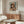 May include: Framed vintage art exhibition poster featuring Renoir's painting of a young girl wearing a pink feathered bonnet and cream dress, displayed on wooden sideboard in minimalist room with white curved chair, glass coffee table, and brass floor lamp