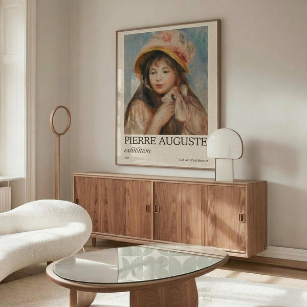 May include: Framed vintage art exhibition poster featuring Renoir's painting of a young girl wearing a pink feathered bonnet and cream dress, displayed on wooden sideboard in minimalist room with white curved chair, glass coffee table, and brass floor lamp