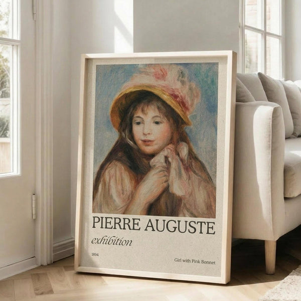 May include: Framed poster print leaning against white wall next to beige sofa in bright living room. Artwork shows young girl in yellow hat with pink feathers, holding small dog, painted in soft impressionist style with warm tones. Exhibition poster format with "PIERRE AUGUSTE" text and "1894" date below painting. Natural sunlight streams through windows onto light wooden floors.