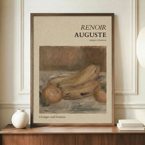 May include: Framed art print featuring a still life painting of oranges and bananas in muted earth tones, displayed on a wooden sideboard beside a white ceramic vase and stacked books. The poster has cream matting with text "RENOIR AUGUSTE" and "oranges et bananes" above and below the artwork. Natural lighting creates soft shadows on the beige wall with white molding.